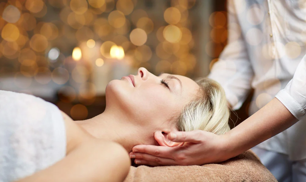 People, beauty, spa, healthy lifestyle and relaxation concept close up of beautiful young woman lying with closed eyes and having head massage in spa
